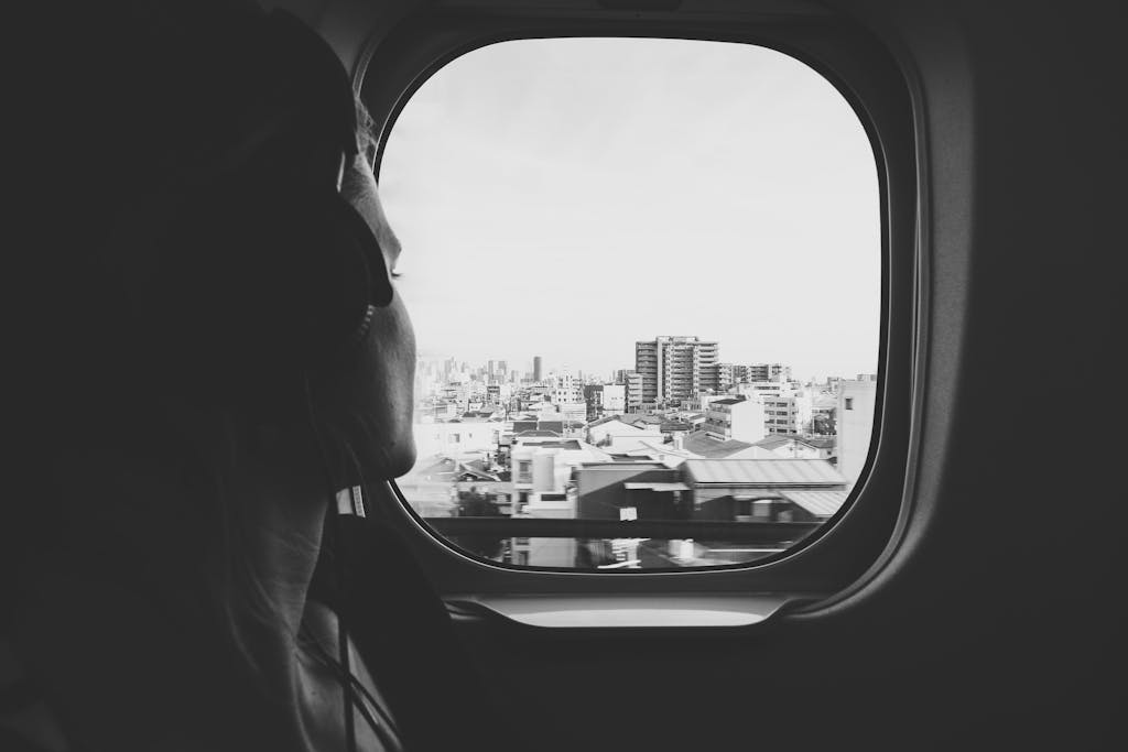 Black and white photo of a woman listening to music while gazing out a train window at the cityscape.